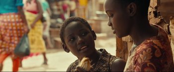 Movie still from “Queen of Katwe” (2016), directed by Mira Nair – A young boy is eating a sandwich while a woman looks on; Close Up shot, Over the shoulder angle