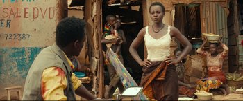 Movie still from “Queen of Katwe” (2016), directed by Mira Nair – A woman standing in front of an easel in front of other people; Medium shot, Over the shoulder angle