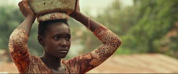 Movie still from “Queen of Katwe” (2016), directed by Mira Nair – A young woman carrying a pot on top of her head; Close Up shot, Over the shoulder angle