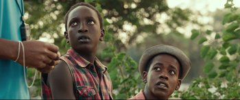 Movie still from “Queen of Katwe” (2016), directed by Mira Nair – Two young men standing next to each other in front of a tree; Close Up shot, Low angle