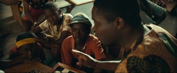 Movie still from “Queen of Katwe” (2016), directed by Mira Nair – A group of young men sitting around a table; Medium shot, Over the shoulder angle