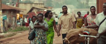 Movie still from “Queen of Katwe” (2016), directed by Mira Nair – A group of people walking down a street holding hands; Medium shot, Over the shoulder angle