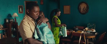 Movie still from “Queen of Katwe” (2016), directed by Mira Nair – A man holding a baby and a woman carrying a bag; Medium shot, Over the shoulder angle
