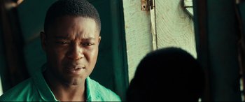 Movie still from “Queen of Katwe” (2016), directed by Mira Nair – A man with a green shirt is standing in front of a door; Close Up shot, Over the shoulder angle
