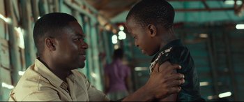 Movie still from “Queen of Katwe” (2016), directed by Mira Nair – A man and a boy are holding each other's hands; Close Up shot, Over the shoulder angle