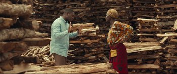 Movie still from “Queen of Katwe” (2016), directed by Mira Nair – A man and a woman standing in front of a pile of wood; Medium shot, Over the shoulder angle