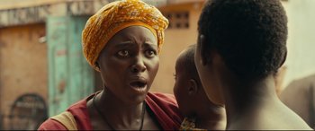 Movie still from “Queen of Katwe” (2016), directed by Mira Nair – A woman with a yellow head scarf is holding a baby; Close Up shot, Over the shoulder angle
