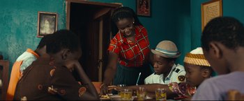 Movie still from “Queen of Katwe” (2016), directed by Mira Nair – A woman standing at a table with two children; Medium shot, Over the shoulder angle