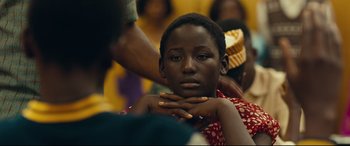 Movie still from “Queen of Katwe” (2016), directed by Mira Nair – A woman sitting in front of a crowd of people; Close Up shot, Over the shoulder angle