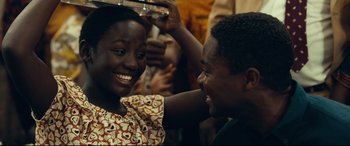 Movie still from “Queen of Katwe” (2016), directed by Mira Nair – Two people are laughing together at a party; Close Up shot, Over the shoulder angle