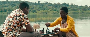 Movie still from “Queen of Katwe” (2016), directed by Mira Nair – Two people sitting on a boat playing a game of chess on the water; Medium shot, High angle