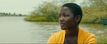 Movie still from “Queen of Katwe” (2016), directed by Mira Nair – A woman sitting in front of a body of water; Close Up shot, Low angle