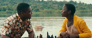 Movie still from “Queen of Katwe” (2016), directed by Mira Nair – Two people sitting next to a body of water; Medium shot, Over the shoulder angle