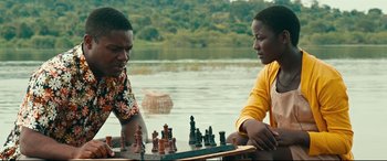 Movie still from “Queen of Katwe” (2016), directed by Mira Nair – Two men playing chess on a river bank; Medium shot, Over the shoulder angle