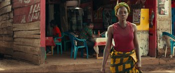 Movie still from “Queen of Katwe” (2016), directed by Mira Nair – A woman standing in front of a group of people sitting at a table; Medium shot, Over the shoulder angle
