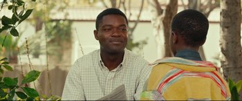 Movie still from “Queen of Katwe” (2016), directed by Mira Nair – A man sitting in front of another man holding a book; Close Up shot, Over the shoulder angle