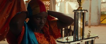 Movie still from “Queen of Katwe” (2016), directed by Mira Nair – A woman in a colorful dress sitting at a table; Close Up shot, Over the shoulder angle
