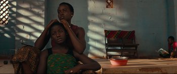 Movie still from “Queen of Katwe” (2016), directed by Mira Nair – A woman sitting next to another woman in a room; Medium shot, Over the shoulder angle