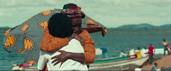 Movie still from “Queen of Katwe” (2016), directed by Mira Nair – Two people hug in front of a body of water; Medium shot, Over the shoulder angle