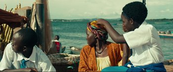 Movie still from “Queen of Katwe” (2016), directed by Mira Nair – A woman sitting on a boat with another woman standing next to her; Medium shot, Over the shoulder angle