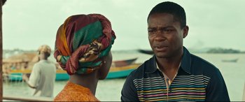 Movie still from “Queen of Katwe” (2016), directed by Mira Nair – A man and a woman are standing next to each other in front of a body of water; Close Up shot, Over the shoulder angle