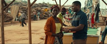 Movie still from “Queen of Katwe” (2016), directed by Mira Nair – A woman standing next to a man in a market; Medium shot, Over the shoulder angle