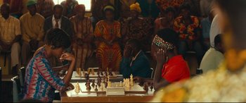 Movie still from “Queen of Katwe” (2016), directed by Mira Nair – A group of people sitting around a table playing chess; Medium shot, Over the shoulder angle