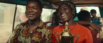 Movie still from “Queen of Katwe” (2016), directed by Mira Nair – A man and a woman smile while holding a trophy; Medium shot, Over the shoulder angle