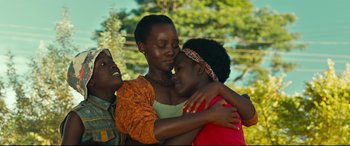 Movie still from “Queen of Katwe” (2016), directed by Mira Nair – A woman and two children hugging each other in front of trees; Close Up shot, Low angle