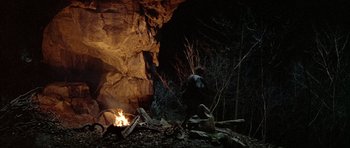 Movie still from “Quest for Fire” (1981), directed by Jean-Jacques Annaud – A man standing in front of a fire in a cave; Wide shot, Low angle