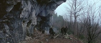 Movie still from “Quest for Fire” (1981), directed by Jean-Jacques Annaud – A group of people standing under a rock formation; Wide shot, Low angle