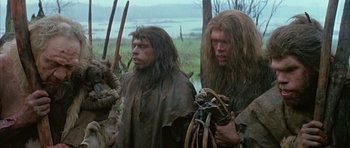 Movie still from “Quest for Fire” (1981), directed by Jean-Jacques Annaud – A couple of people that are standing in the grass; Medium shot, Low angle