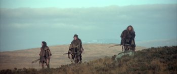 Movie still from “Quest for Fire” (1981), directed by Jean-Jacques Annaud – A group of people dressed as cavemen walking across a field; Wide shot, Low angle