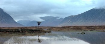 Movie still from “Quest for Fire” (1981), directed by Jean-Jacques Annaud – A person holding an umbrella over their head in the middle of a field; Extreme Wide shot, High angle