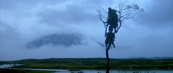 Movie still from “Quest for Fire” (1981), directed by Jean-Jacques Annaud – A dead tree in the middle of a field with mountains in the background; Extreme Wide shot, Low angle