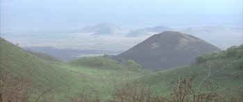Movie still from “Quest for Fire” (1981), directed by Jean-Jacques Annaud – A view of a green valley with mountains in the background; Extreme Wide shot, High angle
