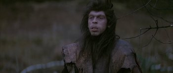 Movie still from “Quest for Fire” (1981), directed by Jean-Jacques Annaud – A man with long black hair and a werewolf costume; Close Up shot, Low angle