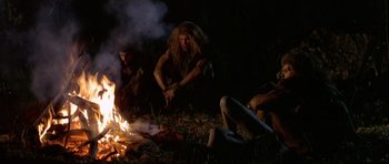 Movie still from “Quest for Fire” (1981), directed by Jean-Jacques Annaud – A group of people sitting around a fire at night; Wide shot, Low angle