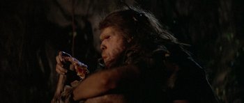 Movie still from “Quest for Fire” (1981), directed by Jean-Jacques Annaud – A person eating a piece of pizza; Close Up shot, Low angle