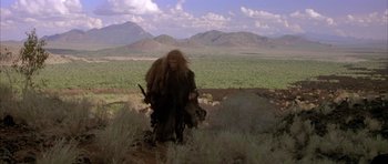 Movie still from “Quest for Fire” (1981), directed by Jean-Jacques Annaud – A man in a long coat standing in a field; Wide shot, Low angle