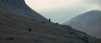 Movie still from “Quest for Fire” (1981), directed by Jean-Jacques Annaud – A person sitting on top of a grass covered hill; Extreme Wide shot, Low angle