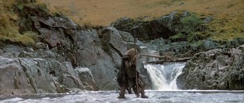 Movie still from “Quest for Fire” (1981), directed by Jean-Jacques Annaud – A man with a spear standing in the water near a waterfall; Wide shot, Low angle
