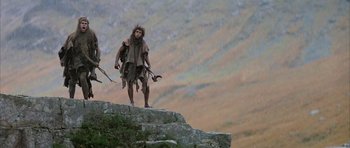 Movie still from “Quest for Fire” (1981), directed by Jean-Jacques Annaud – A man standing on top of a mountain holding a spear; Wide shot, Low angle