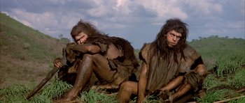 Movie still from “Quest for Fire” (1981), directed by Jean-Jacques Annaud – A couple of people that are sitting in the grass; Medium shot, Low angle