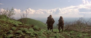 Movie still from “Quest for Fire” (1981), directed by Jean-Jacques Annaud – A couple of people standing on top of a grass covered hill; Wide shot, Low angle
