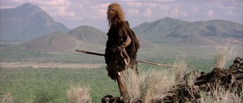 Movie still from “Quest for Fire” (1981), directed by Jean-Jacques Annaud – A man dressed as a caveman standing on top of a hill; Wide shot, Low angle