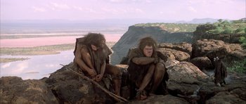 Movie still from “Quest for Fire” (1981), directed by Jean-Jacques Annaud – A couple of people sitting on top of a rock; Wide shot, Low angle
