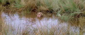 Movie still from “Quest for Fire” (1981), directed by Jean-Jacques Annaud – A man in a body of water surrounded by tall grass; Wide shot, High angle
