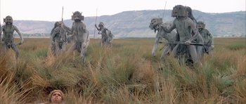 Movie still from “Quest for Fire” (1981), directed by Jean-Jacques Annaud – A group of statues in a field of tall grass; Extreme Wide shot, High angle