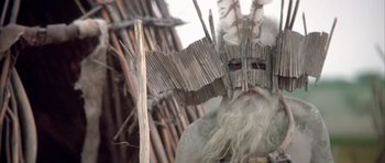 Movie still from “Quest for Fire” (1981), directed by Jean-Jacques Annaud – An old man with long white hair and a mask; Close Up shot, Low angle